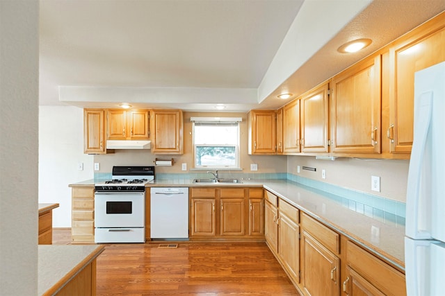 kitchen with light wood-type flooring, a sink, under cabinet range hood, white appliances, and light countertops