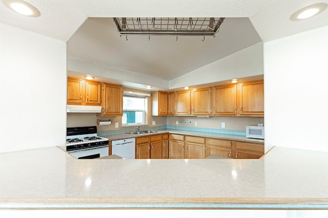 kitchen featuring a sink, under cabinet range hood, white appliances, a peninsula, and vaulted ceiling