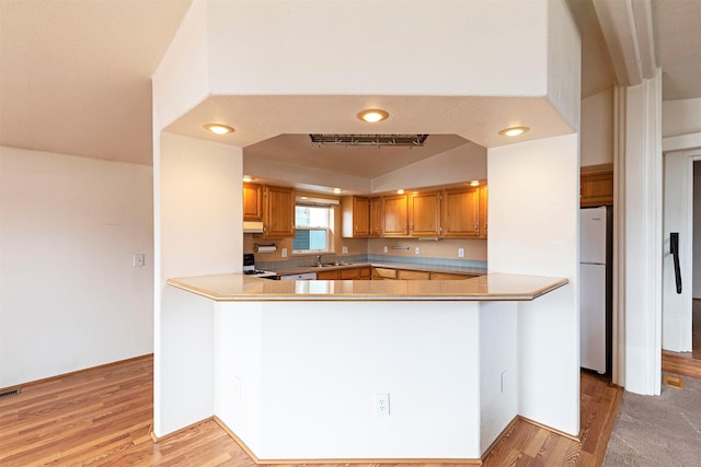 kitchen featuring under cabinet range hood, light wood-type flooring, a peninsula, freestanding refrigerator, and a sink