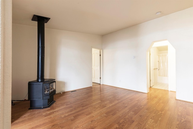 unfurnished living room featuring visible vents, arched walkways, wood finished floors, and a wood stove