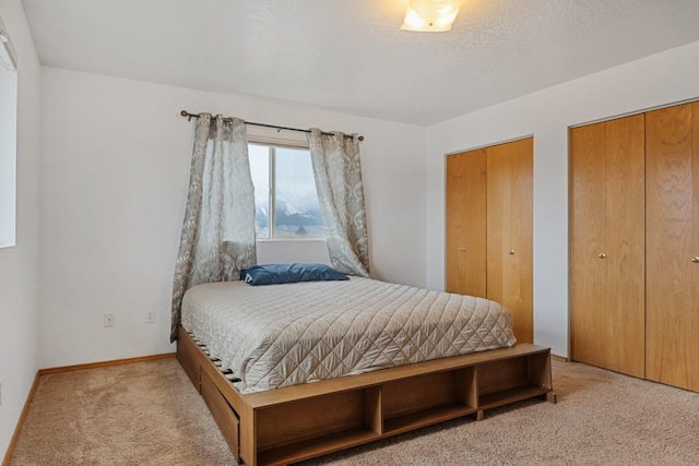 bedroom with baseboards, two closets, and carpet flooring