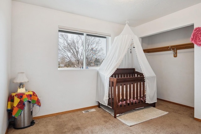 carpeted bedroom with a closet, visible vents, a crib, and baseboards