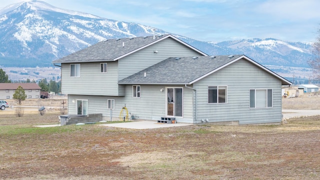 rear view of house with a patio area, a mountain view, and a shingled roof