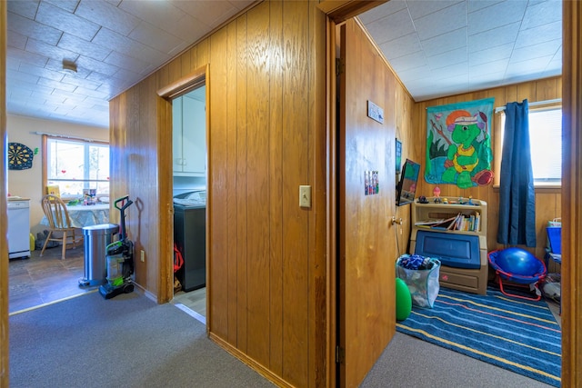 hallway with washer / dryer, wood walls, and carpet floors