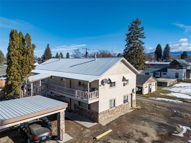 view of property exterior with a balcony, stone siding, driveway, and metal roof