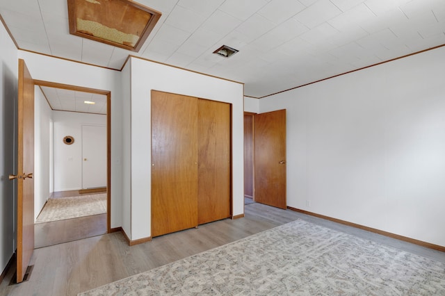 unfurnished bedroom featuring a closet, crown molding, baseboards, and wood finished floors