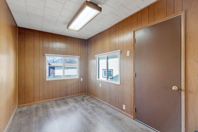 unfurnished room featuring baseboards, wood walls, and light wood finished floors