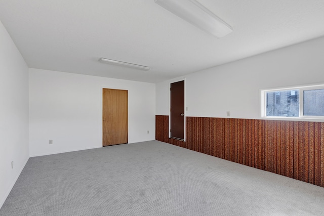 carpeted empty room with wooden walls and a wainscoted wall