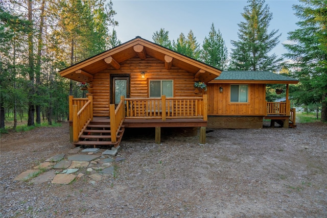 view of front of house with a wooden deck, roof with shingles, and log exterior