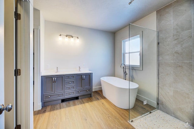 full bath featuring a sink, wood finished floors, double vanity, baseboards, and a soaking tub