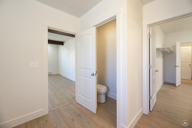 corridor with baseboard heating, beamed ceiling, baseboards, and light wood-style floors