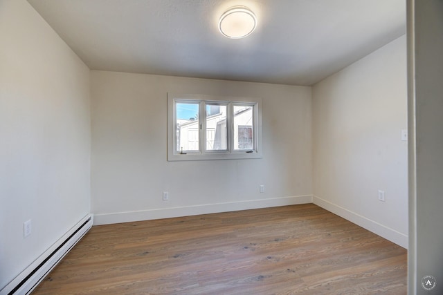 empty room featuring wood finished floors, baseboards, and a baseboard radiator