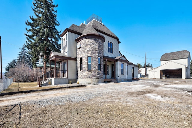 view of front of property featuring a garage, stone siding, an outbuilding, and fence