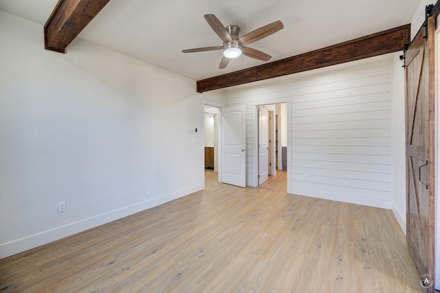 spare room with a ceiling fan, baseboards, beam ceiling, light wood-style floors, and a barn door