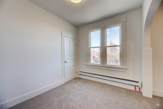 carpeted spare room with a baseboard heating unit, arched walkways, and baseboards