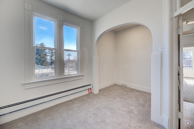 empty room featuring arched walkways, light colored carpet, and a baseboard heating unit