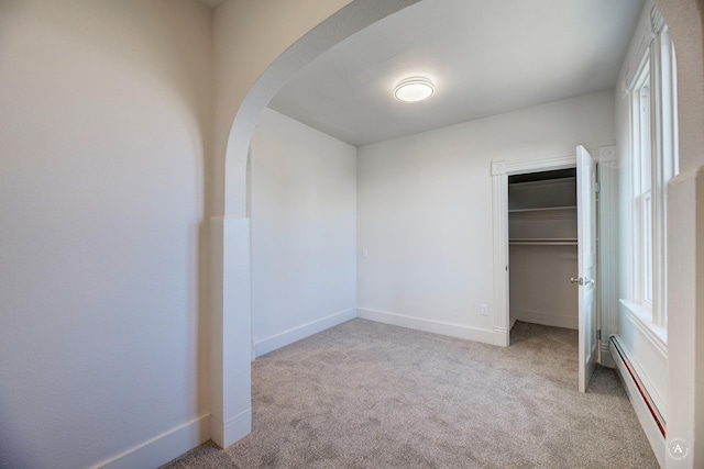 unfurnished bedroom featuring baseboards, carpet, a closet, arched walkways, and a baseboard radiator