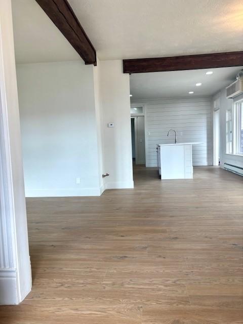 unfurnished living room with light wood-type flooring, beam ceiling, baseboards, and a baseboard heating unit