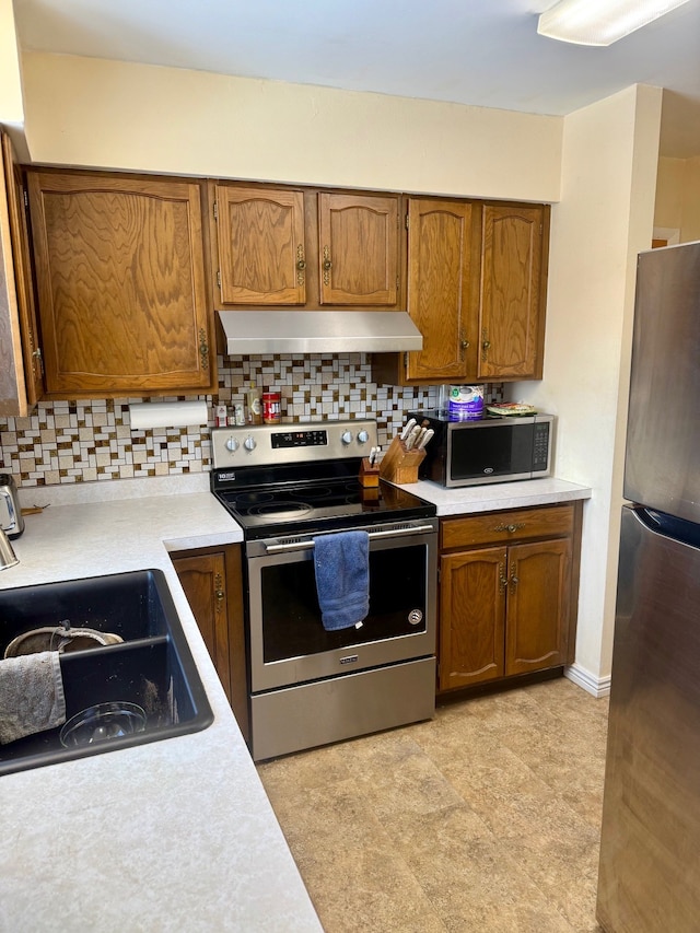 kitchen with tasteful backsplash, under cabinet range hood, light countertops, stainless steel appliances, and a sink