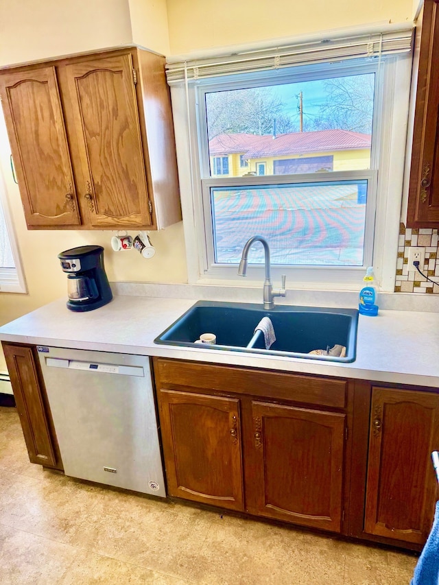 kitchen with light countertops, decorative backsplash, brown cabinets, stainless steel dishwasher, and a sink