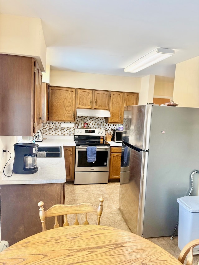 kitchen with under cabinet range hood, a sink, backsplash, appliances with stainless steel finishes, and light countertops