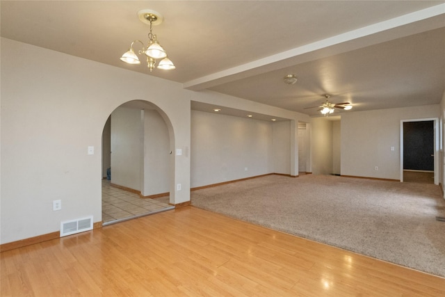 unfurnished room with wood finished floors, visible vents, baseboards, arched walkways, and ceiling fan with notable chandelier