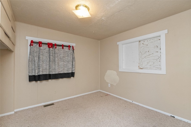 unfurnished room with baseboards, carpet, visible vents, and a textured ceiling