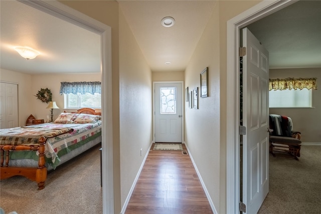 hallway featuring carpet flooring, wood finished floors, and baseboards