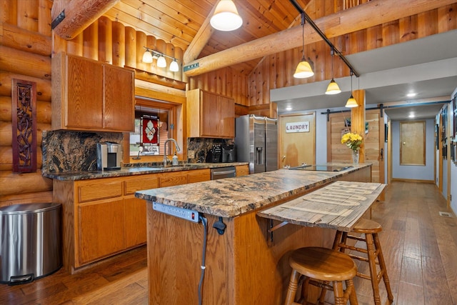 32 Peaceful Ct, Bigfork, MT 59911 - kitchen with appliances with stainless steel finishes, vaulted ceiling, brown cabinetry, dark wood-style floors, and rustic walls