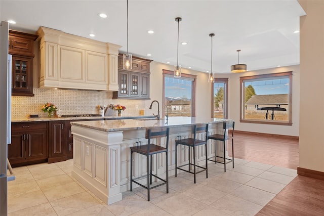 kitchen featuring a kitchen bar, a sink, light stone counters, cream cabinets, and glass insert cabinets