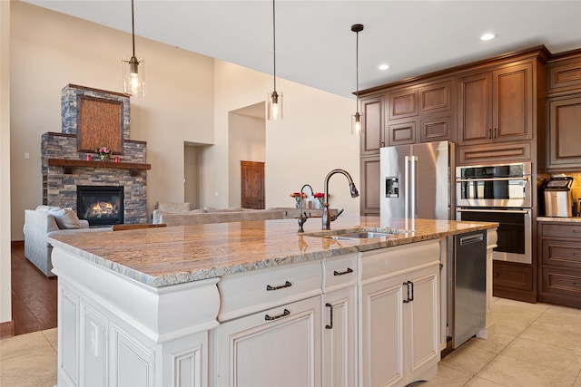 kitchen with a kitchen island with sink, a sink, appliances with stainless steel finishes, a fireplace, and light stone countertops