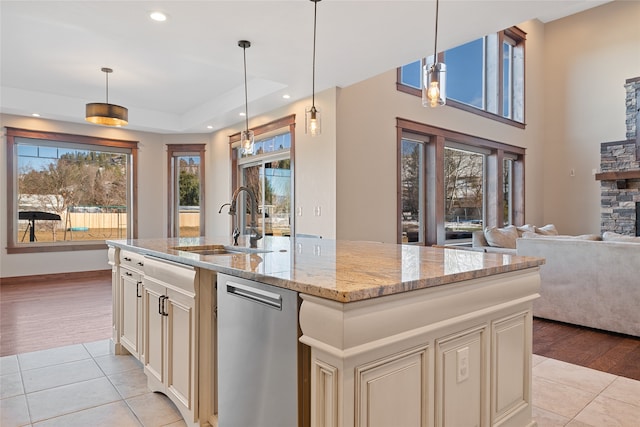 kitchen with light tile patterned floors, a sink, cream cabinetry, stainless steel dishwasher, and open floor plan