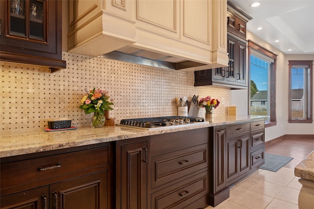 kitchen with dark brown cabinetry, cream cabinetry, glass insert cabinets, and custom range hood