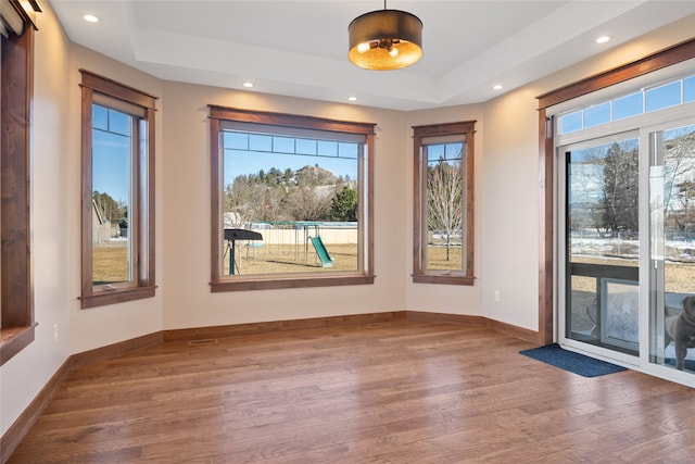 interior space featuring recessed lighting, baseboards, a raised ceiling, and wood finished floors