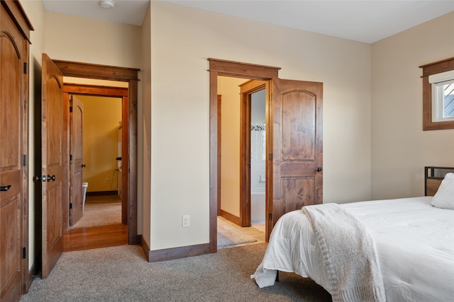 bedroom with light colored carpet, ensuite bathroom, and baseboards