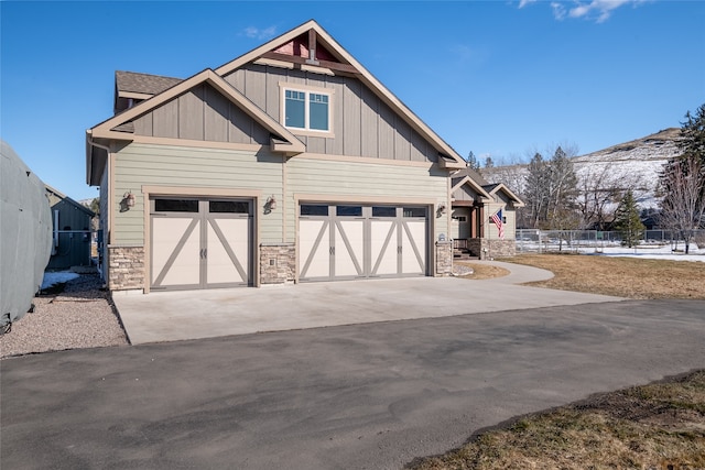 exterior space featuring board and batten siding, concrete driveway, fence, and stone siding