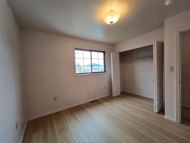 unfurnished bedroom with light wood finished floors, visible vents, baseboards, and a closet