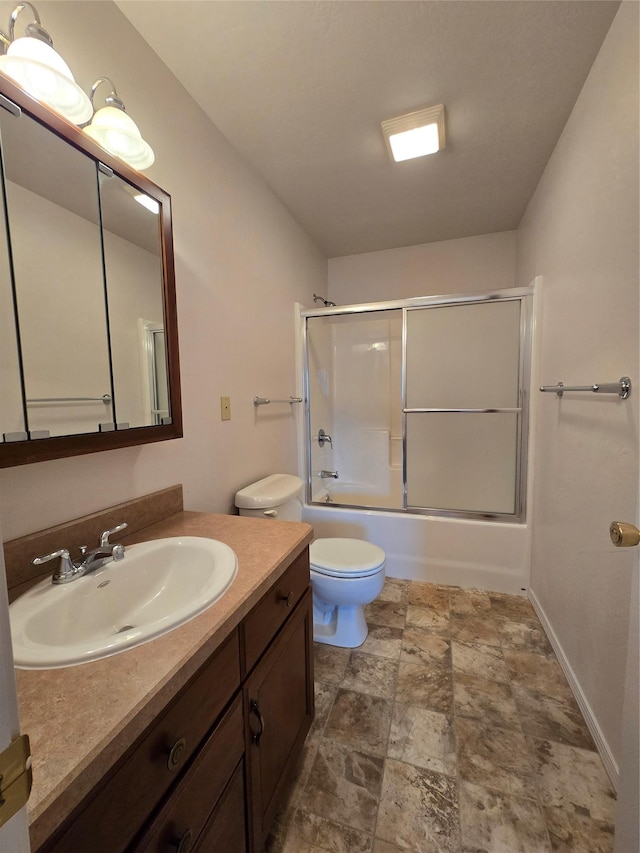 full bath featuring vanity, baseboards, shower / bath combination with glass door, stone finish flooring, and toilet