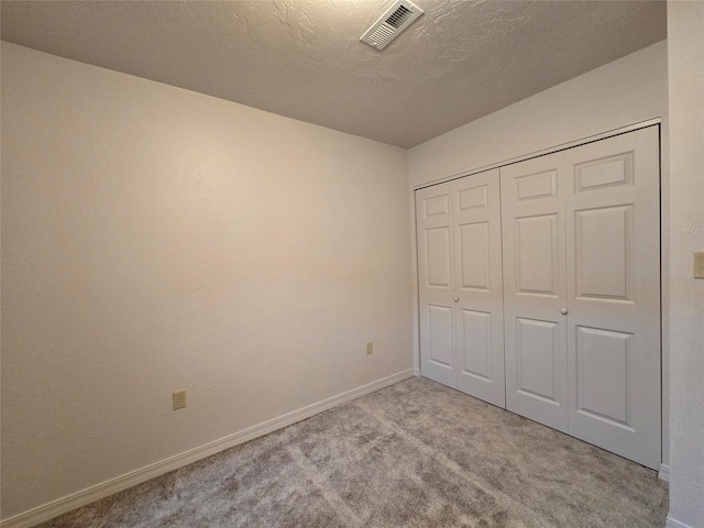 unfurnished bedroom with carpet, visible vents, baseboards, a closet, and a textured ceiling