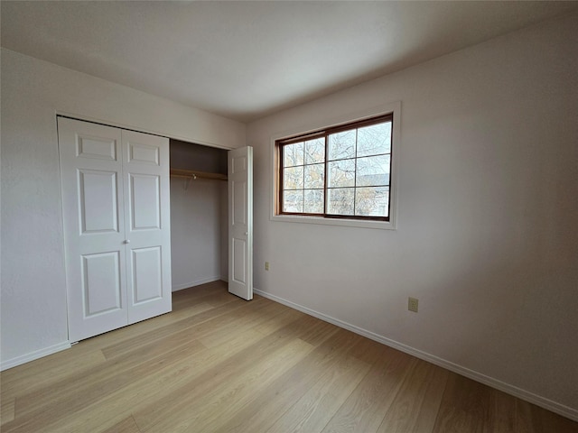 unfurnished bedroom featuring light wood-style floors, baseboards, and a closet