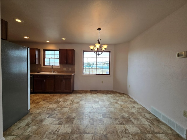 kitchen featuring visible vents, light countertops, freestanding refrigerator, a notable chandelier, and a sink