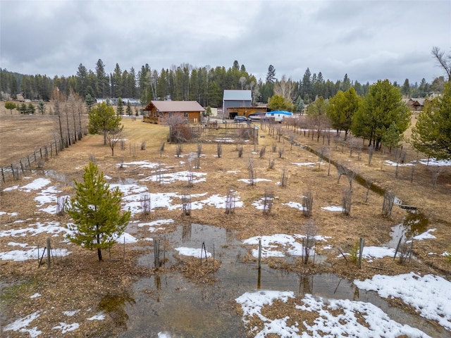 snowy yard with a rural view, a forest view, and fence