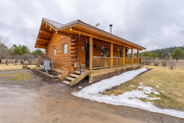 view of front facade with log exterior, fence, covered porch, and metal roof