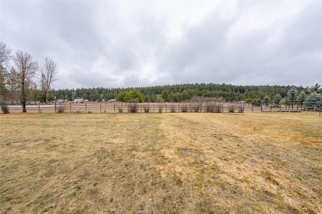 view of yard with a rural view, a wooded view, and fence