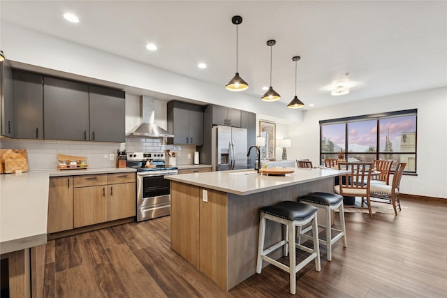 kitchen featuring light countertops, decorative backsplash, stainless steel appliances, wall chimney exhaust hood, and a sink