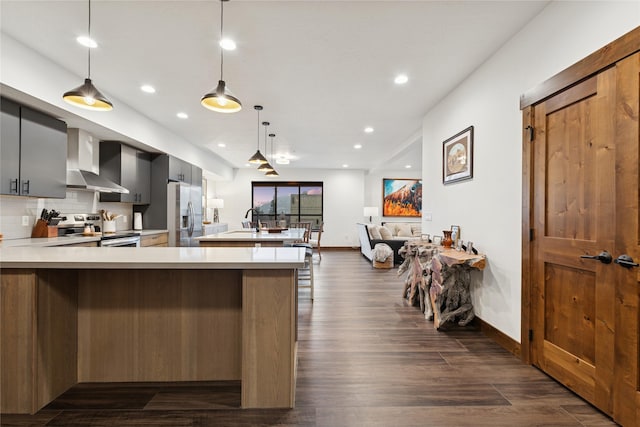 kitchen with dark wood-type flooring, light countertops, decorative backsplash, appliances with stainless steel finishes, and wall chimney exhaust hood