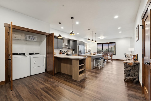 kitchen with washing machine and clothes dryer, dark wood-style flooring, stainless steel appliances, light countertops, and wall chimney range hood