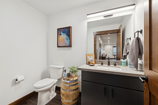 bathroom with vanity, toilet, wood finished floors, and baseboards