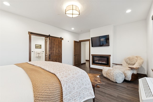 bedroom with dark wood finished floors, a barn door, recessed lighting, and a glass covered fireplace