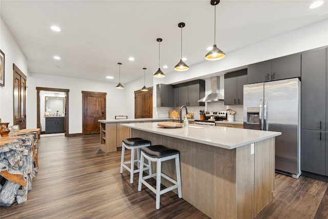 kitchen with light countertops, wall chimney range hood, an island with sink, and stainless steel appliances